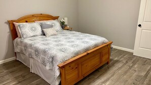 A wooden bed with a patterned bedspread and matching pillows, a nightstand with a lamp and a vase of flowers, and a wooden floor. - Twin Oaks Cozy Getaway in Lake Charles (Lake Charles)