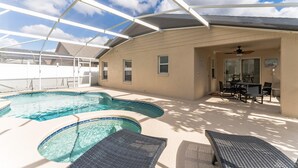Un área de piscina exterior techada con sillones reclinables, una mesa y un ventilador de techo.