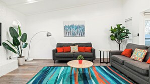 A modern living room with a grey sofa, a round coffee table, a colorful striped rug, and a large plant. - Near Highways, Family Friendly, Garage, Foosball, Grill, Dart, Tesla Charger (Plano)