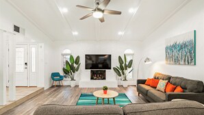 A living room with a fireplace, a ceiling fan, and a large TV. - Near Highways, Family Friendly, Garage, Foosball, Grill, Dart, Tesla Charger (Plano)