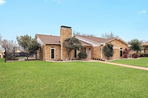 A two-story house with a brick exterior, a chimney, and a well-maintained lawn. - Near Highways, Family Friendly, Garage, Foosball, Grill, Dart, Tesla Charger (Plano)