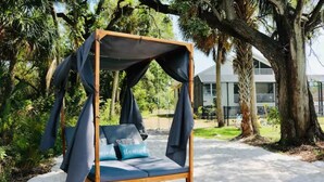 A wooden swing bed with a canopy, surrounded by trees and a building in the background. - Casa Azul Tampa - 5BR Waterfront Villa w/ Pool (Tampa)