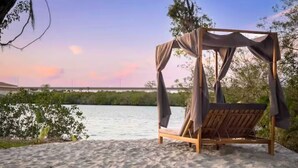 A beach setting with a wooden canopy bed and a view of the water. - Casa Azul Tampa - 5BR Waterfront Villa w/ Pool (Tampa)