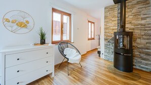 Una sala de estar moderna con una pared de piedra, una estufa de leña negra, un aparador blanco y una silla.