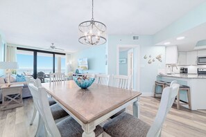 A dining area with a large wooden table, white chairs, a blue decorative bowl, and a chandelier.