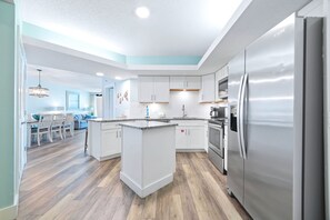 Una cocina moderna con armarios blancos, un refrigerador de acero inoxidable y suelo de madera.