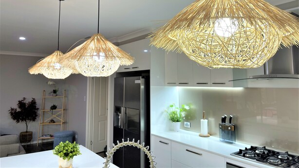 Une cuisine moderne avec des meubles blancs, une cuisinière à gaz et un luminaire suspendu en fibres tressées.