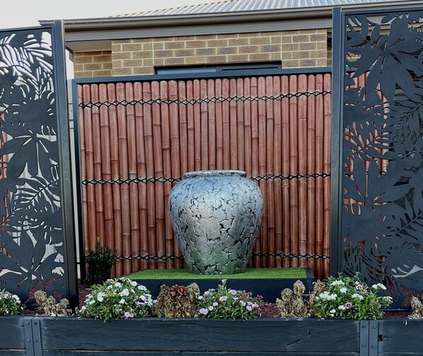 Ein großer, dekorativer Blumentopf in einem Garten mit Bambuszaun und Metalltoren.