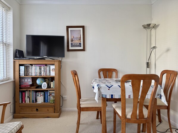 Un salon chaleureux avec un téléviseur posé sur un meuble en bois, une bibliothèque remplie de livres, un tableau encadré accroché au mur et une table à manger avec des chaises.