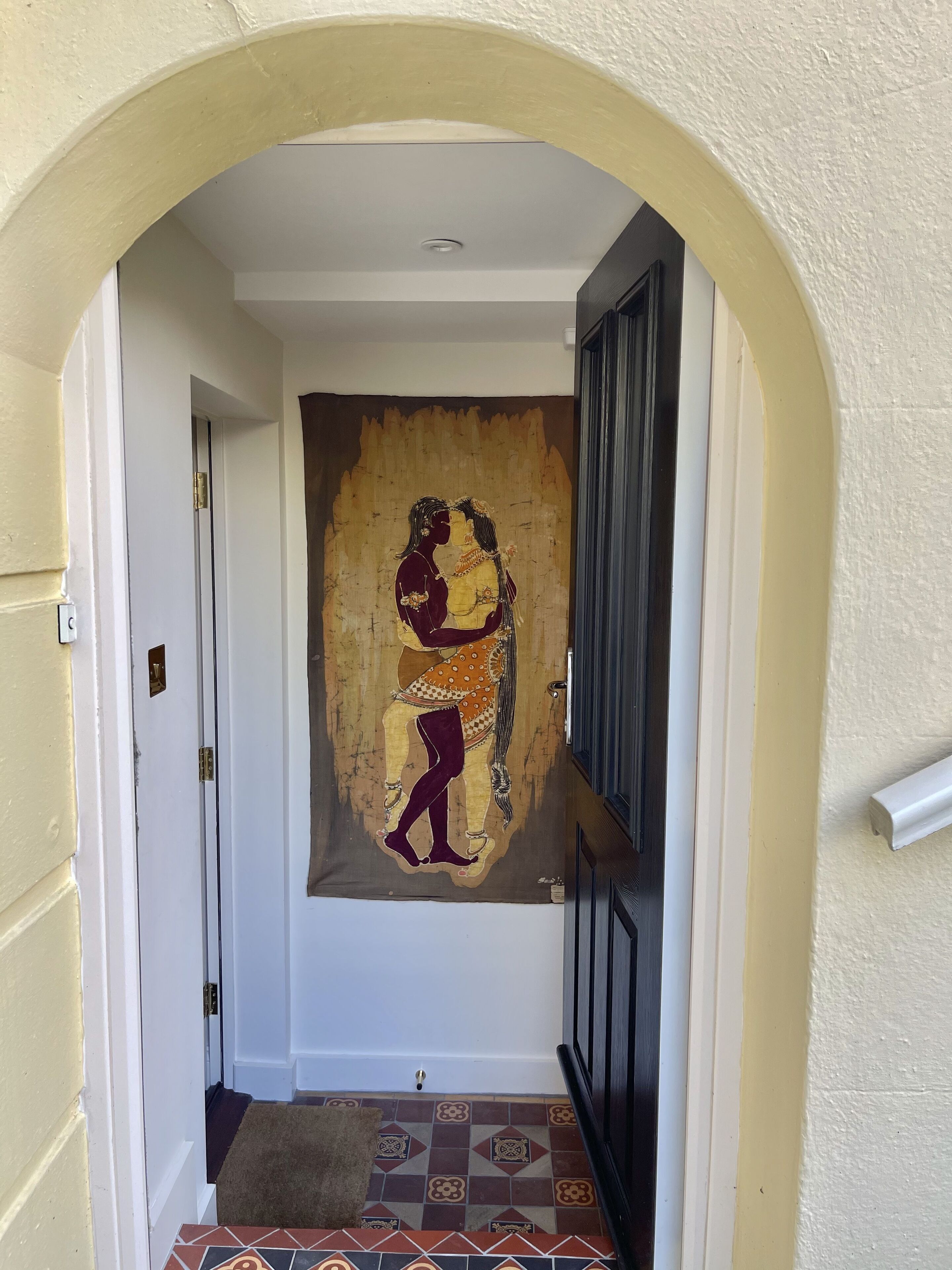 A hallway with a tapestry depicting a couple, a door, and a patterned rug.