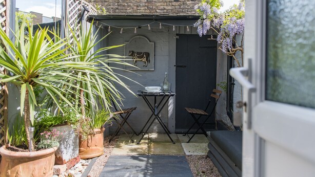 A small patio area with potted plants, a table, and chairs.