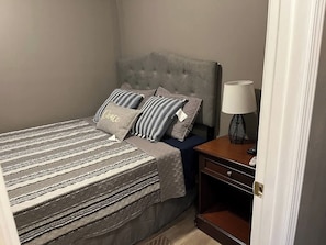 A bedroom with a bed, pillows, a nightstand, a lamp, and a door.
