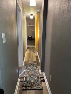 A hallway with a patterned rug, wooden flooring, and a door leading to a room.