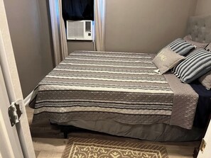 A bedroom with a bed, pillows, a rug, and an air conditioning unit.