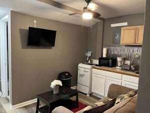 A compact living space with a kitchenette, a flat-screen TV, a ceiling fan, and a dining area.