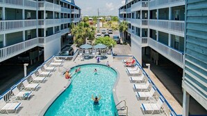 Une piscine entourée de chaises longues et un bâtiment doté de balcons.