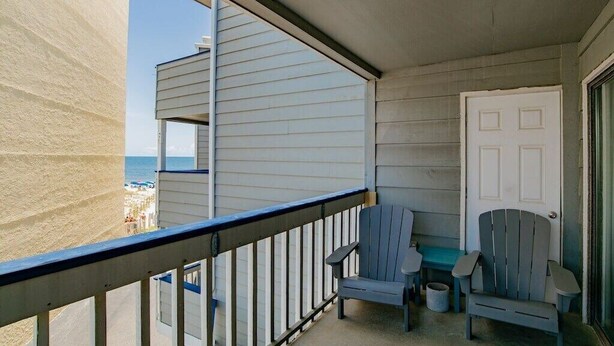 Un balcon avec deux fauteuils Adirondack, une petite table et une porte.