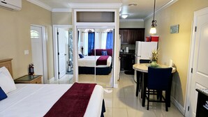 Ein Hotelzimmer mit Bett, Schreibtisch, Stuhl, kleinem Tisch und einer Küchenzeile.