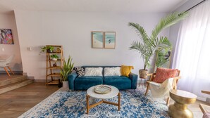 Un salon avec un canapé bleu, une table basse ronde, un tapis à motifs et une bibliothèque agrémentée de plantes.