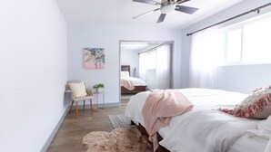 Une chambre à coucher avec un lit, une chaise, une petite table avec une plante et un tableau accroché au mur.