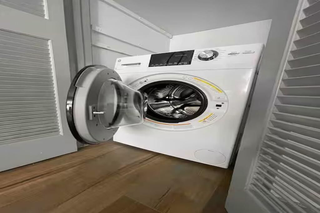 Una lavadora de carga frontal en un cuarto de lavado con piso de madera y paredes blancas.