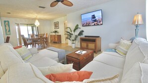 Ein Wohnzimmer mit Deckenventilator, Fernseher, Essbereich mit Stühlen und einer Couch mit Kissen.