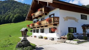 A traditional Alpine building with balconies, a sign reading "Fronywiesen," and a scenic mountain backdrop.