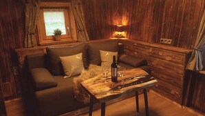 A cozy room with a wooden interior, a sofa, a table with a bottle and glasses, and a window with curtains.