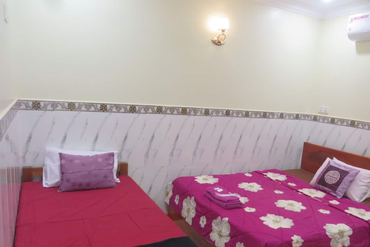 Un dormitorio con dos camas, una con cubrecama rojo y la otra con cubrecama rosa y flores blancas. Hay un aire acondicionado de pared y un aplique.
