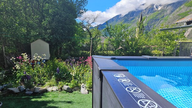 Une piscine agrémentée d’un panneau de sécurité, entourée d’un jardin luxuriant et avec une chaîne de montagnes en toile de fond.