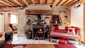 Une pièce chaleureuse avec une cheminée en pierre, des poutres apparentes, un canapé et un lit avec une literie rouge et blanche.