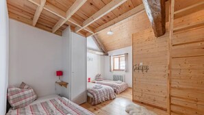 Une pièce chaleureuse avec des poutres apparentes, deux lits avec une literie à rayures, un tapis moelleux et une petite fenêtre.