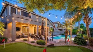 Una casa moderna con piscina, mobiliario de exterior e iluminación con luces colgantes.