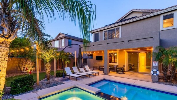 Una casa moderna con piscina, mobiliario exterior y un patio bien iluminado.