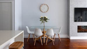 A modern dining area with a glass table, white chairs, and a wooden floor. - Two Plus Two Modern Retreat in Middle Park (Middle Park)