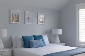 Quarto com cama, duas mesas de cabeceira e três quadros na parede.