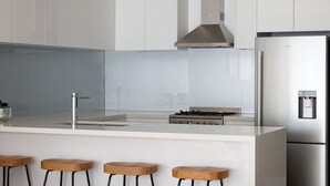 A modern kitchen with white cabinets, a stainless steel range hood, a built-in gas stove, a refrigerator, and wooden bar stools. - Two Plus Two Modern Retreat in Middle Park (Middle Park)