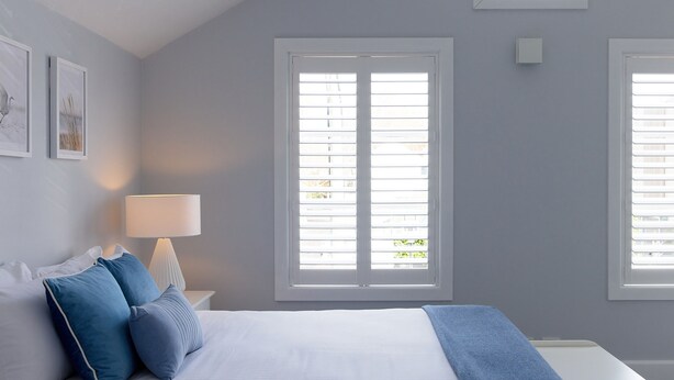 A bedroom with a bed, pillows, a nightstand, a lamp, and two windows with blinds. - Two Plus Two Modern Retreat in Middle Park (Middle Park)