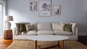 A living room with a sofa, a round coffee table, and three framed beach photographs on the wall. - Two Plus Two Modern Retreat in Middle Park (Middle Park)