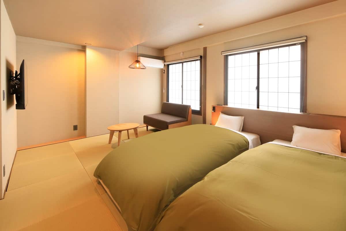 A hotel room with two beds, a sofa, a small table, and a TV.