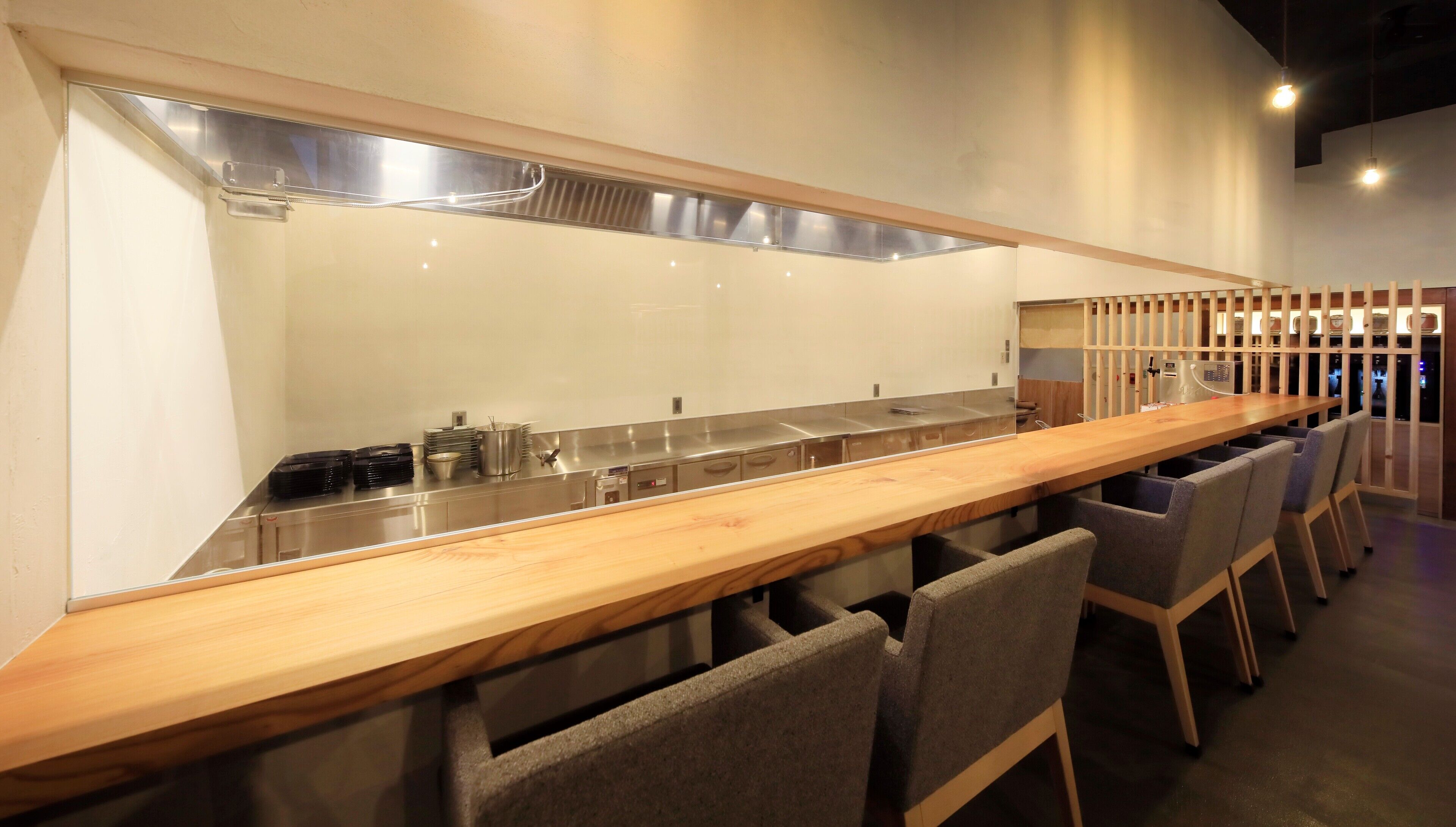 A long wooden counter with a stainless steel sink and a row of chairs.