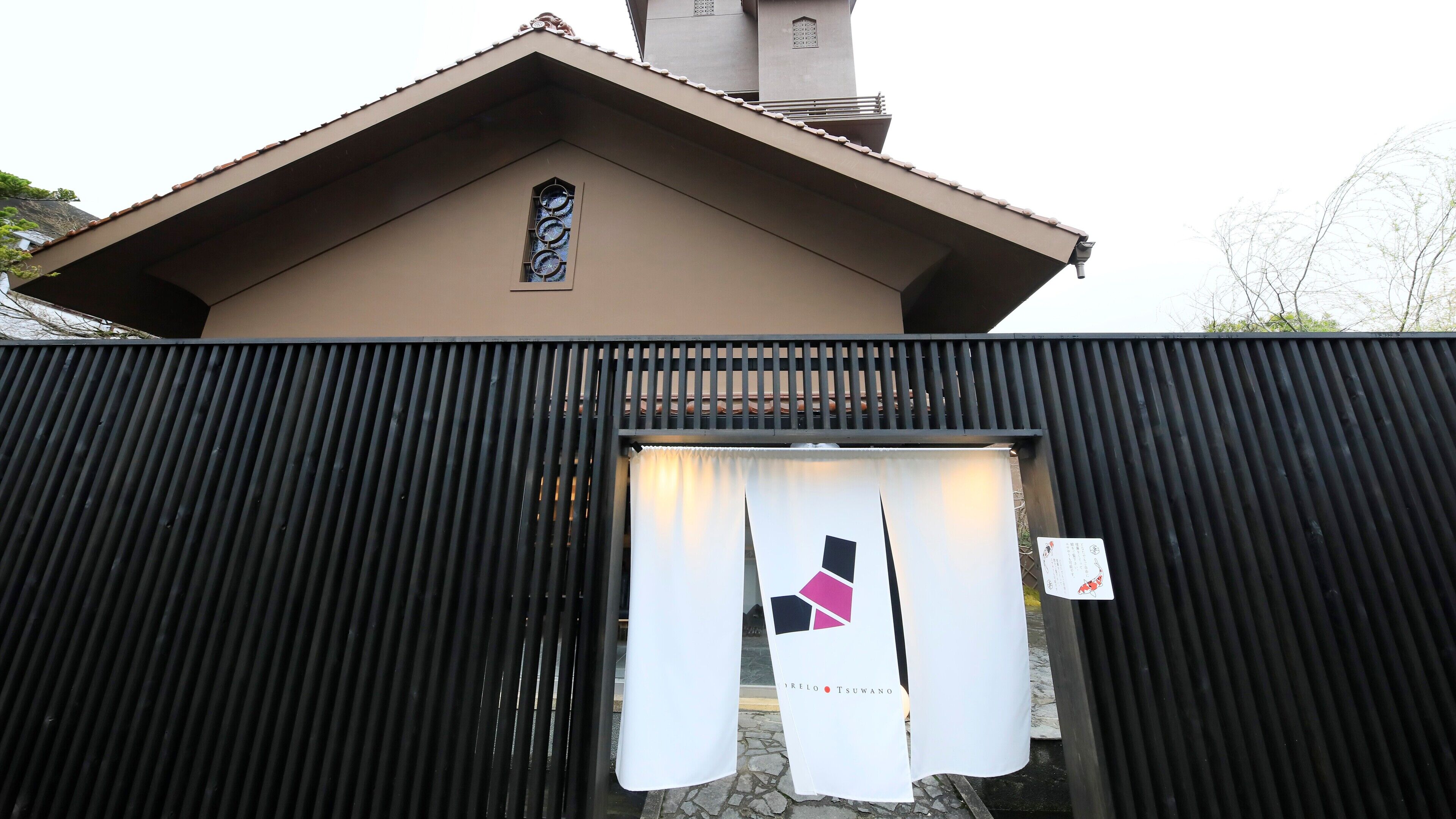 A building with a brown facade, a window with a decorative grille, and a black corrugated metal fence.