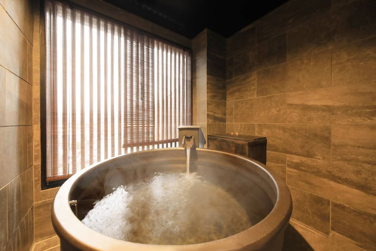 A hot tub with water flowing, surrounded by stone walls and a window with vertical blinds.