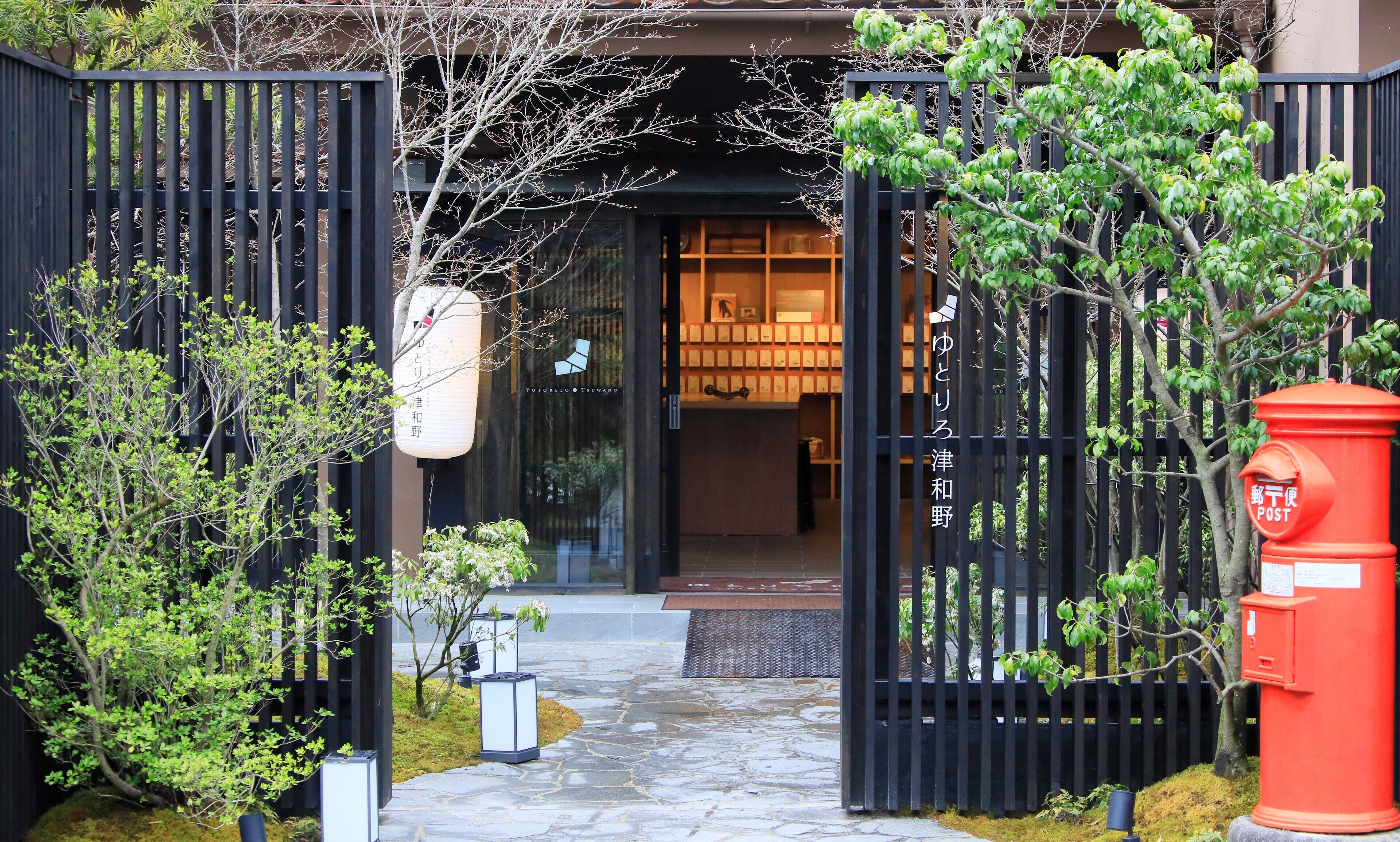 Edificio japonés tradicional con una verja negra, sendero de piedra y un buzón rojo.