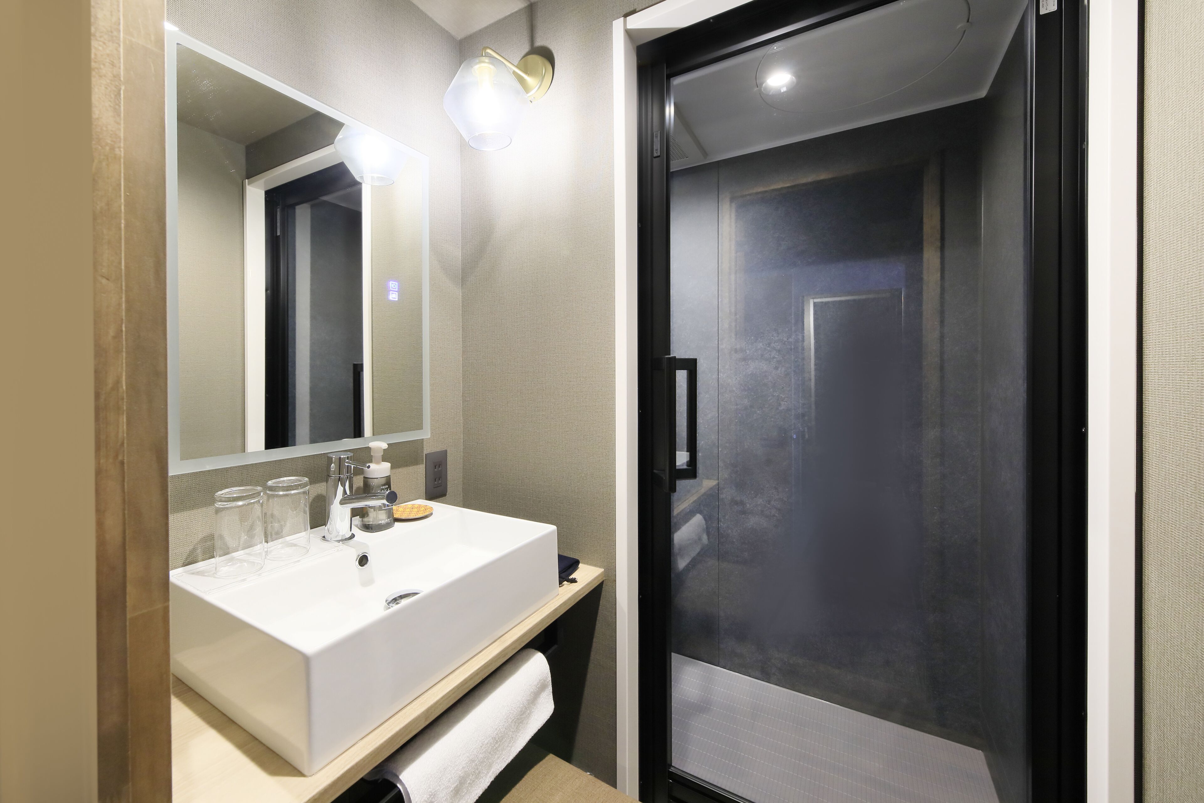 A modern bathroom with a white sink, mirror, and glass shower enclosure.