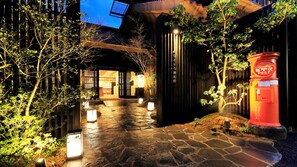 A stone pathway leading to a traditional Japanese building with lanterns and a red post box.