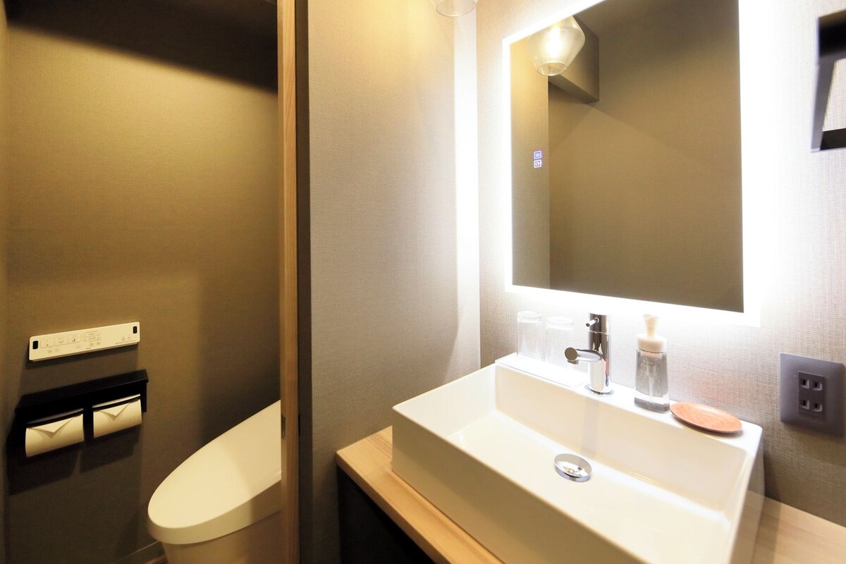 Un baño con inodoro, lavamanos con espejo y una lámpara en la pared.