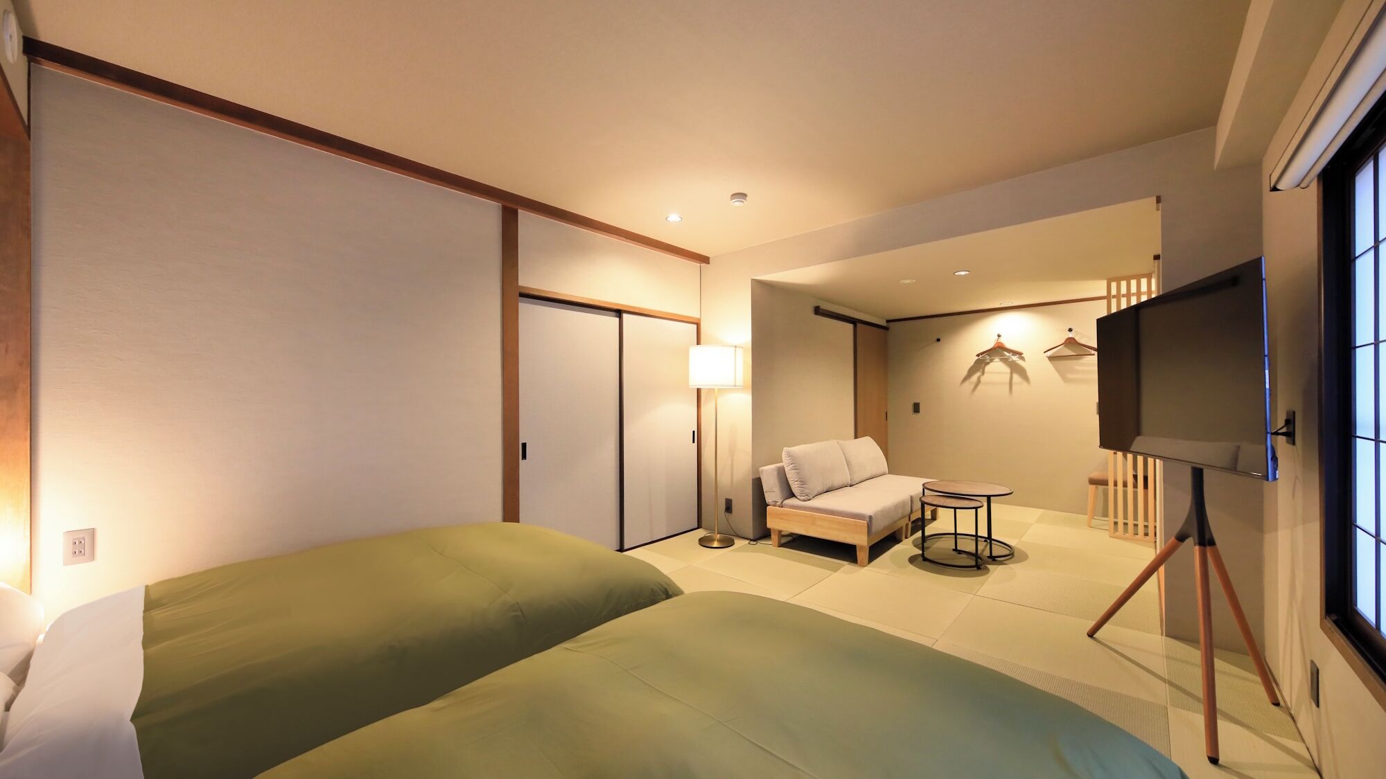 Une chambre d’hôtel avec deux lits, un canapé, une petite table, une télévision et une armoire.