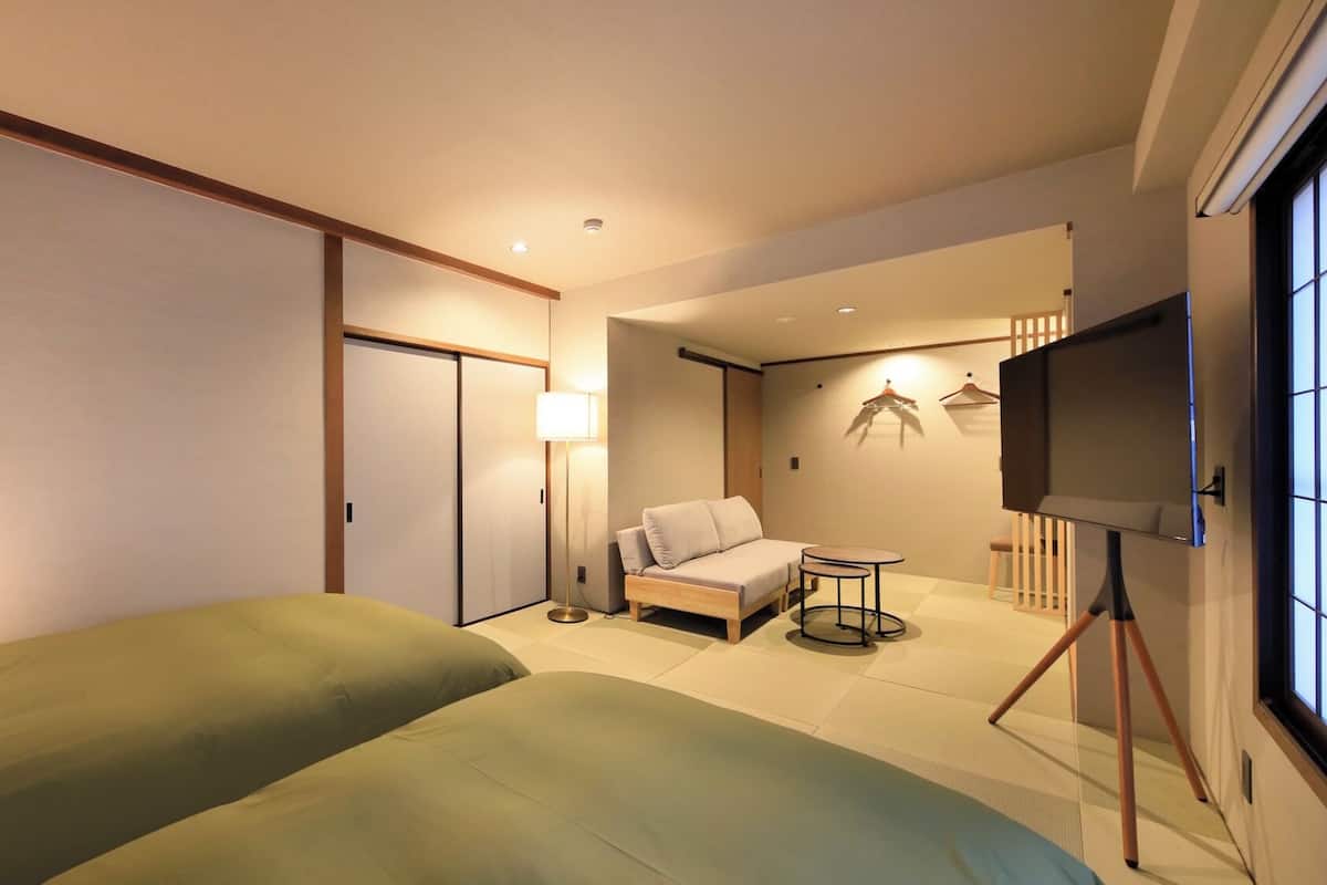 A hotel room with two beds, a sofa, a small table, a TV, and a wardrobe.