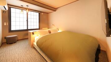 A hotel room with a bed, bedside table, lamp, window, and a small stool.